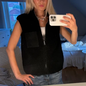 Fleeceväst - Mysig svart fleeceväst med krage och hel dragkedja framtill. Västen har en fyrkantig bröstficka och är tillverkad i mjukt teddyfleece-material. Perfekt att slänga över en hoodie eller t-shirt för extra värme. Enkel och stilren design som funkar till det mesta💞