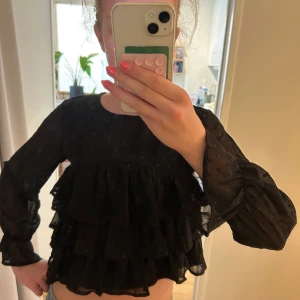 Svart volangblus från Gina Tricot - Supersöt svart blus från Gina Tricot med prickigt mönster och flera lager volanger. Långärmad modell i tunn, luftig polyester med lätt transparenta ärmar och rund hals. Perfekt för dig som gillar statement-plagg och volanger! Passar till fester och högtider ❤️jag är 164cm som referens. Skriv vid övriga funderingar 🥰