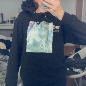 Svart hoodie Common Kollectiv XS - Svart hoodie från Common Kollectiv i storlek XS. Tröjan har en stor färgglad print framtill, snörning vid huvan och klassisk känguruficka. Perfekt för dig som gillar streetstyle och vill ha en chill look.