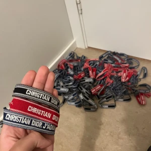3 stycken, Christian Dior broderade armband - Broderade armband från Christian Dior i olika färger: svart, röd och marinblå. Armbanden har texten 'CHRISTIAN DIOR' eller 'CHRISTIAN DIOR J'ADIOR' och avslutas med snygga tofsar. Perfekt accessoar för att lyfta din outfit med en lyxig touch.
