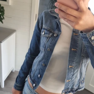 Blå jeansjacka i klassisk modell - Säljer en klassisk blå jeansjacka från Denim i storlek 36. Jackan har snygga sömmar, knappar framtill och två bröstfickor. Perfekt att slänga över en t-shirt för en chill och tidlös look.