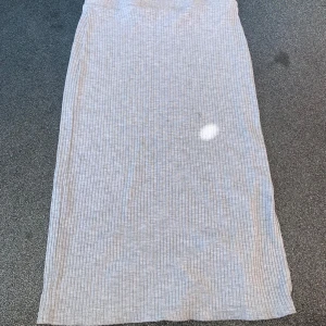 Ljusgrå ribbad långkjol med slits - Säljer en ljusgrå ribbad långkjol med diskreta vertikala ränder och en snygg slits på sidan. Kjolen är mjuk och stretchig, perfekt för en chill och stilren look. Passar dig som gillar enkel men trendig stil.