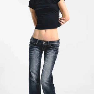 Svarta lågmidjade bootcut jeans - Säljer ett par svarta bootcut jeans med låg midja och snygga slitningar framtill. Jeansen har klassiska fem fickor, markerade sömmar och coola detaljer på bakfickorna. Perfekta för dig som gillar 00-talsvibbar och vill ha en relaxed look. Ser mer svarta än de 3 första bilder. Aldrig använt, säljer pga fel storlek. Pris går absolut diskuteras. Passar XS-S-M