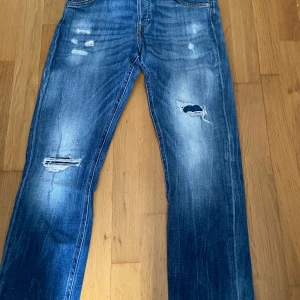Blå slitna jeans 30/30 - Säljer ett par blå jeans med slitningar och hål på knäna. Jeansen har klassisk femficksdesign, raka ben och snyggt tvättad denim. Perfekta för dig som gillar en avslappnad och trendig look.