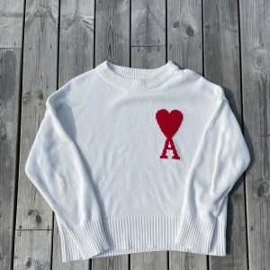 Vit stickad tröja från Ami Paris - Vit stickad tröja från Ami Paris med röd logga. Tröjan har en lös passform och har storleken M.