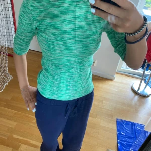 Grön ribbad topp med trekvartsärm - Säljer en grön ribbad topp med trekvartsärm. Toppen har ett diskret mönster i olika gröna nyanser och sitter tight mot kroppen. Perfekt för dig som gillar en fräsch och färgglad stil. Materialet är stretchigt och bekvämt.