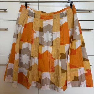 Magisk mönstrad kjol i bomull från Orla Kiely, fodrad, storlek 1/ 36 - Superfin kjol från Orla Kiely med magiskt mönster i orange, gul, beige, brun och vitt. Kjolen går till knät, har veck och dragkedja bak. Tillverkad i bomull och är fodrad. En liten skada i tyget som syns på bild14 och en svag fläck som syns på bild 5. Ej märkbara när den bärs.