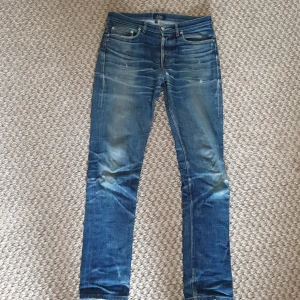 A.P.C. New Standard blå jeans, stl 29 - Säljer ett par klassiska A.P.C. New Standard jeans i blå tvätt med snyggt slitna detaljer och whiskers. Jeansen har rak passform, fem fickor och orange kontrastsömmar. Materialet är robust denim i bomull. Perfekta för dig som gillar en clean men avslappnad look.