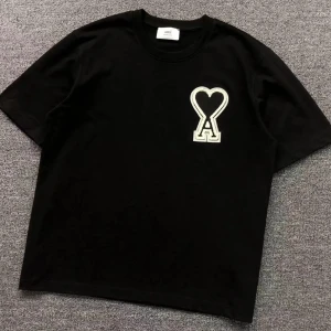 Svart t-shirt från Ami Paris med hjärtdetalj - Svart t-shirt från Ami Paris med korta ärmar och en stor vit broderad logga med hjärta och bokstaven A på bröstet. Klassisk rund halsringning och avslappnad passform. Perfekt för en stilren och trendig look.