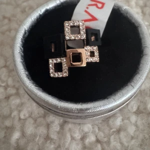 Ny. Statementring med fyrkantiga detaljer - Cool ring med flera fyrkantiga former i guld, svart och glittrande stenar. Ringen har en unik design med både matta och blingiga rutor som ger en modern och edgy vibe. Perfekt accessoar för att sticka ut och lyfta din stil.