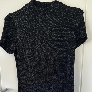 Glittrig svart topp från Monki - Säljer en svart glittrig topp från Monki i storlek S🖤 Toppen har korta ärmar, hög hals och är täckt av små silvriga glitterprickar🖤Materialet är stretchigt 🖤 säljer pga att den inte kommer till användning🖤 normal i storlek