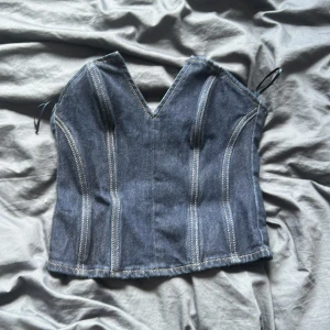 Jeans-korsett från Zara XS - Snygg jeans-korsett från Zara i mörkblå denim med markerade sömmar och v-ringad hals. Toppen är ärmlös och har dragkedja bak för enkel påklädning. Perfekt att styla med kjol eller byxor för en cool look.