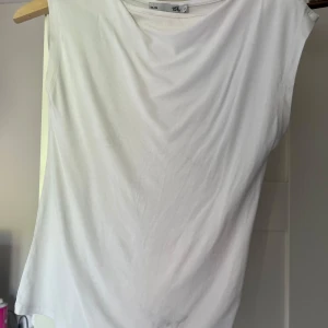 Vit ärmlös boatneck topp från 157, XS - Enkel och stilren vit topp från 157 i storlek XS. Modellen är ärmlös med rund halsringning och rak passform. Perfekt att matcha med jeans eller kjol för en clean look. Gjord i mjukt bomullsmaterial som känns skönt mot huden. Kan vara lite sminkfläck högst upp