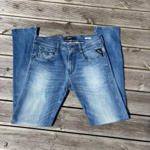 Replay Anbass blå jeans, stl 30/32 - Säljer ett par Replay Anbass jeans i klassisk blå tvätt med snygga slitningar och dragkedja. Modellen har fem fickor, slim passform och raka ben. Perfekta för dig som gillar en stilren och avslappnad look. Kom gärna med frågor!🙌 