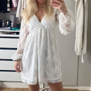 Vit blommig kortklänning från Gina Tricot - Superfin vit klänning från Gina Tricot med broderade blommor, v-ringning och långa transparenta ärmar. Klänningen har en lös passform och knytning i ryggen. Perfekt för sommarens alla tillfällen men framför allt till student och skolavslutning. Så fin studentklänning. Nypris är 800kr