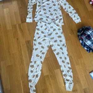 Vita mjukisbyxor med bakelsemönster - Säljer ett par vita mjukisbyxor med gulligt bakelsemönster i brunt och beige. Byxorna har resår i midjan och är tillverkade i mjukt bomullsmaterial, perfekta för att chilla hemma. Matchar toppen om du vill ha ett helt set!