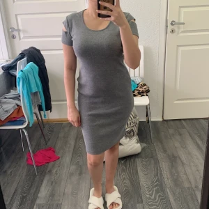 Grå tight klänning med cut out-detaljer - Säljer en grå tight klänning med korta ärmar och snygga cut out-detaljer på axlarna. Klänningen är enkel men stilren och har en rund halsringning. Perfekt för dig som gillar en minimalistisk look.