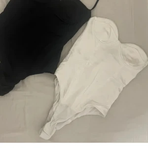vit bodysuit topp -  bodysuits i vitt med bygel och formade kupor. Perfekt att styla med jeans eller kjol för en trendig look. Axelbandslös design som ger en snygg siluett.