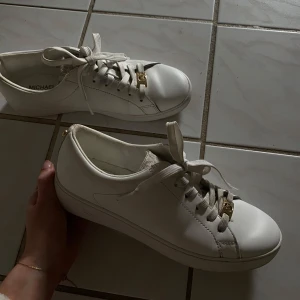 Mikael Kors skor - Säljer ett par vita sneakers från Michael Kors med gulddetaljer på snörningen och logotyp på plösen. Annvända ca 10 gånger men var för små för mig!❤️köpta för 1700 men säljer för 800, priset går såklart att diskutera!