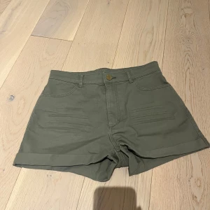Olivgröna shorts från H&M - Snygga shorts från H&M i en färg som skriker sommar. Shortsen har klassisk femficksdesign och uppvikta benslut. De har normal passform, bälteshällor och stängs med knapp och dragkedja. Perfekta för varma dagar. Supersnygga till sommaren.🤩