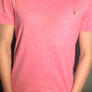 Rosa t-shirt från Polo Ralph Lauren - Säljer en rosa t-shirt från Polo Ralph Lauren med klassisk broderad logga på bröstet. T-shirten har korta ärmar och en slim fit passform. Perfekt för dig som gillar stilrena och bekväma plagg. Desutom så är priset verkligen inte fast spikat i väggen. Hör av er vid minsta fundering, ingen fråga är dum så fråga på vi svarar på allt inom kort🔥🥂