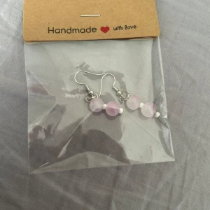 Handgjorda örhängen med rosa pärlor - Säljer ett par handgjorda örhängen med två ljusrosa pärlor och små vita detaljer. Krokar i silverfärgad metall. Perfekta för att ge en söt och personlig touch till din stil.💕🫶🏼