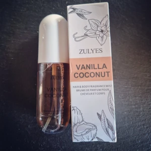 Zulye's Vanilla Coconut Hair & Body Fragrance Mist - En söt och tropisk doftmist för hår och kropp från Zulye's med doft av vanilj och kokos. Flaskan är genomskinlig med vit kork och kommer i en stilren förpackning med blommigt och kokosnötsmotiv. Perfekt för dig som älskar fräscha och exotiska dofter. Endast testsprayad.