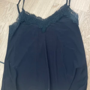 Svart linnetopp med spets  - Säljer en svart linnetopp från New Yorker med tunna axelband och vacker spetsdetalj längs urringningen. Perfekt att styla till olika outfits för en trendig look.
