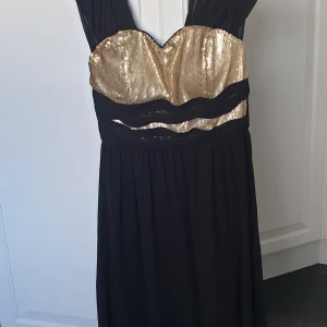 Svart och guldig  balklänning från Pink Boom - Säljer en elegant balklänning från Pink Boom i svart med glittrig guldig överdel och vågiga paljett-detaljer. Klänningen har breda axelband och markerad midja, perfekt för festliga tillfällen. Materialet känns mjukt och följsamt.