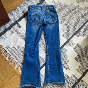 Blå bootcut jeans från Gina Tricot - Säljer ett par klassiska blå jeans från Gina Tricot i modellen bootcut. Jeansen har normal passform, fyra  fickor och snygga sömdetaljer på bakfickorna. Perfekta för dig som gillar en tidlös denimlook.