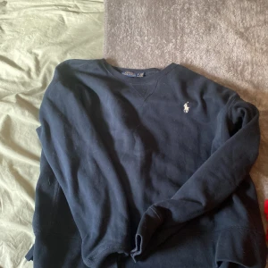 Mörkblå tröja från Polo Ralph Lauren - Säljer en klassisk mörkblå långärmad tröja från Polo Ralph Lauren med broderad logga på bröstet. Tröjan har rund halsringning och är tillverkad i mjuk bomull. Perfekt för en stilren och avslappnad look. Tröjan kommer att tvättas och fixas och bli iordningställd innan den skickas