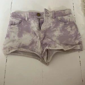 Ljuslila och vita tie-dye shorts från H&M - Säljer ett par ljuslila och vita shorts från H&M med tie-dye mönster. Modellen är kort med normal passform och har klassiska fickor fram och bak samt dragkedja och knapp. Perfekta för sommaren! Tvättar innan jag skickar produkten 💕