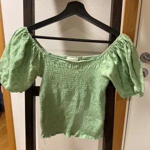 Grön topp med puffärmar från Dobber - Säljer en ljusgrön topp från Dobber med smockad kropp och broderade puffärmar. Toppen har en söt offshoulder-modell och är perfekt för vår och sommar. Ärmarna har fina blommiga broderier som ger en romantisk känsla.