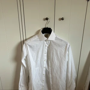 La Chemise skjorta - Klassisk vit skjorta från La Chemise med lång ärm och knappar framtill. Skjortan har en stilren design med krage och är perfekt för en dressad look. Tillverkad i bomull för en bekväm känsla.