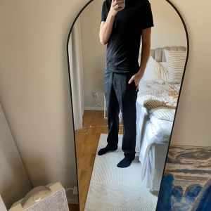 Svarta kostymbyxor - Säljer ett par klassiska svarta kostymbyxor med normal passform. Byxorna har raka ben, hällor för bälte och stängs med dragkedja och knapp. Perfekta för en stilren look.