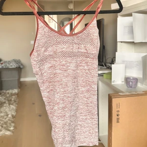 Lila och vit linnetopp med korsade axelband - Säljer en sportig lila och vit linnetopp med smala korsade axelband och meshdetaljer fram och bak. Perfekt för träning eller varma dagar. Snygg och bekväm passform med ventilerande material.