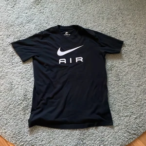 Svart Nike Air t-shirt - Säljer en svart t-shirt från Nike med stor vit Nike-logga och texten 'AIR' på bröstet. Klassisk passform och rund halsringning. Perfekt för en sportig och avslappnad stil. Bra till sommaren och knappt använd. Nypris: 550 kr