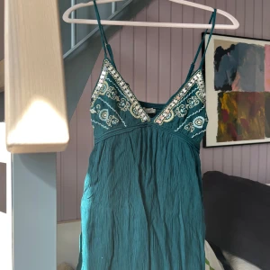 Grön kort klänning med broderade detaljer - Supersöt grön kort klänning med tunna axelband och v-ringning. Överdelen har fina vita broderier 