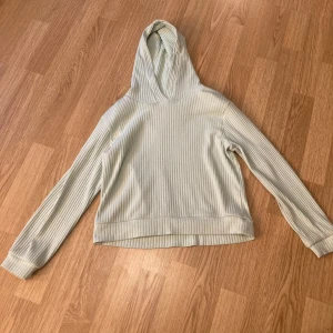 Ljusgrön ribbad hoodie från KappAhl - Säljer en ljusgrön ribbad hoodie från KappAhl i storlek 134/140. Tröjan har långa ärmar, huva och är tillverkad i ett mjukt, ribbat material som ger en skön känsla. Perfekt för en avslappnad stil. 