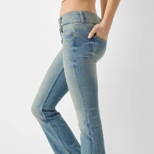 Lågmidjade bootcut jeans i ljusblå denim - Säljer ett par lågmidjade bootcut jeans i ljusblå denim med klassisk femficksdesign och dragkedja. Jeansen har en lätt utsvängd passform nedtill och subtila slitningar framtill för en trendig look.
