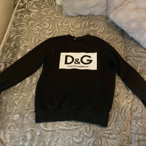 Svart sweatshirt från Dolce & Gabbana - Säljer en svart sweatshirt från Dolce & Gabbana med stor vit logga på bröstet. Tröjan har rund halsringning och långa ärmar. Perfekt för en stilren och trendig look.