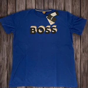 Blå t-shirt från BOSS - Snygg blå t-shirt från BOSS med stort tryck över bröstet. Klassisk rund halsringning och korta ärmar. Perfekt för en stilren och avslappnad look.