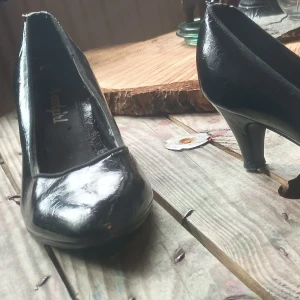 Svarta pumps med klack - Säljer ett par klassiska svarta pumps från Cordial. Skorna har rund tå och medelhög klack, tillverkade i syntetmaterial med glansig finish. Perfekta för dig som gillar en tidlös och stilren look.