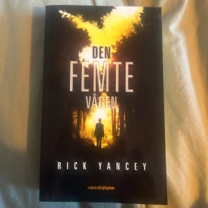 Den femte vågen - Säljer boken 'Den femte vågen' av Rick Yancey. En spännande science fiction-roman om Cassie som kämpar för att överleva efter en utomjordisk attack. Omslaget är svart med en siluett av en person i en upplyst skog. Perfekt för dig som gillar dystopier och äventyr.