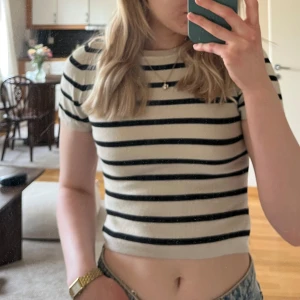 Randig croppad topp från Gina Tricot - Säljer en vit croppad topp från Gina Tricot med svarta horisontella ränder. Toppen har korta ärmar och rund halsringning. Perfekt till jeans eller kjol för en avslappnad stil.