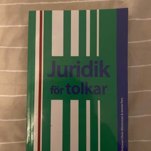 Juridik för tolkar - En bok med grön och blå framsida samt vita och röda ränder. Titeln är 'Juridik för tolkar' och boken riktar sig till tolkar som behöver kunskap om juridik. Perfekt för studier eller yrkesverksamma inom tolkning.