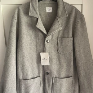 Ljusgrå ulljacka från John Henric - Snygg ljusgrå jacka från John Henric. Storlek XL men passar mer som L. Helt ny skick och aldrig använd.                                          Jackan har knäppning med knappar och en stilren, minimalistisk design som passar perfekt till lager-på-lager.