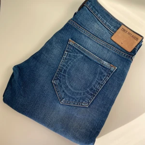 True Religion Jeans - Säljer ett par äkta True Religion jeans i storlek W32. Klassisk modell med snygga detaljer och ikoniska sömmar. Bra skick utan större slitningar eller fläckar. Perfekta för dig som vill ha en stilren men edgy look. Nypris ca 2000–2500 kr.
