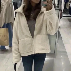 Beige teddyjacka med dragkedja - Mysig beige teddyjacka med dragkedja framtill och stora fickor. Jackan har en hög krage och lång ärm, perfekt för kyligare dagar. Passformen är normal och materialet är fluffigt och mjukt. 