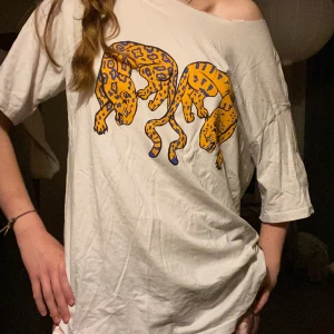 Vit oversized t-shirt med leopardtryck - Vit oversized t-shirt med stort tryck av två tecknade leoparder i gult och blått på framsidan. T-shirten har en avslappnad passform och korta ärmar, perfekt för en chill och trendig look.